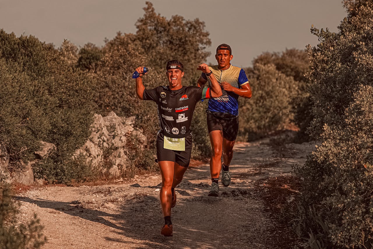 Two athletes express joy during a rural marathon run, surrounded by shrubs.