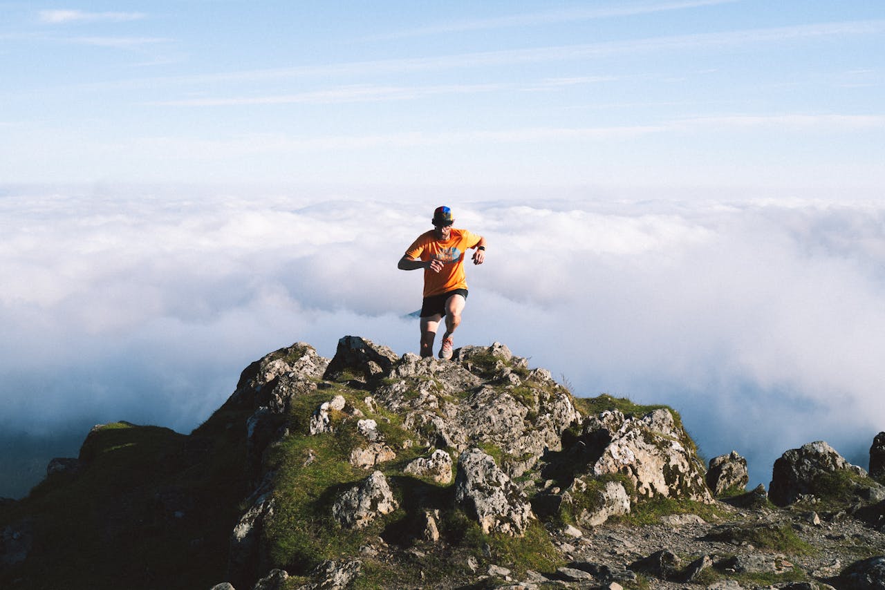 Man running on rocky mountain peak above the clouds, symbolizing achievement and adventure.