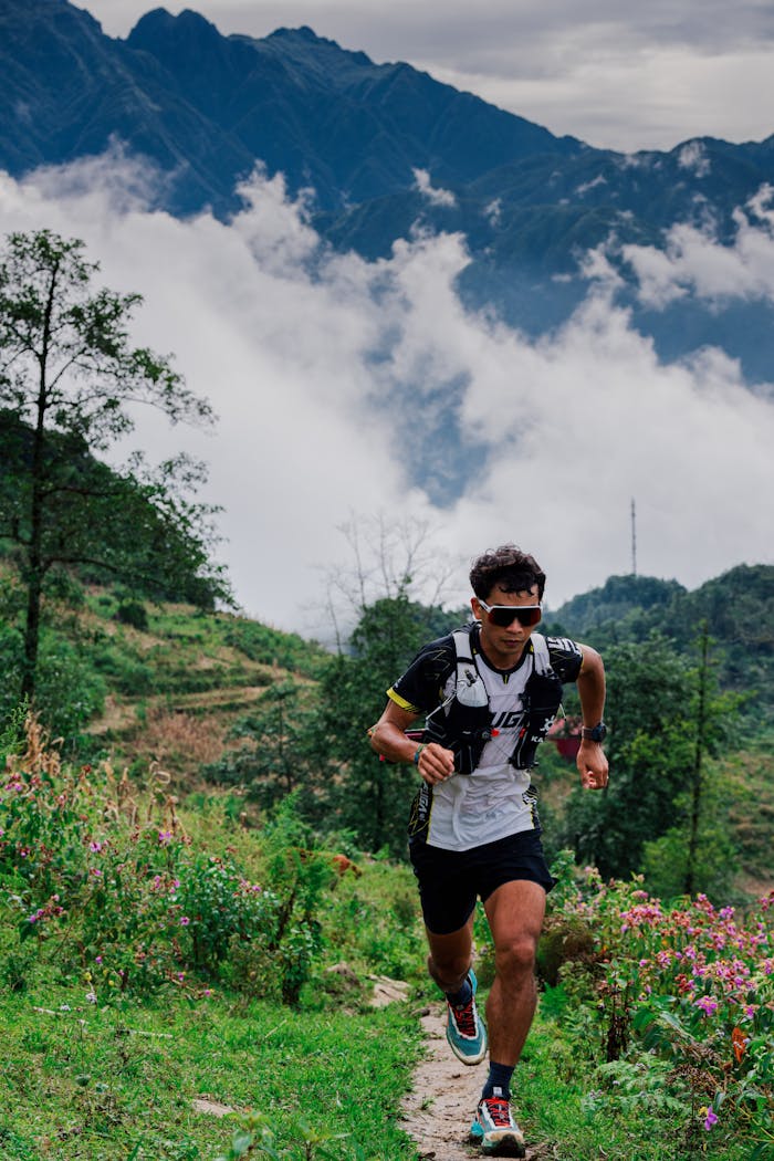 Man running on a mountain trail surrounded by scenic landscapes under cloudy skies.